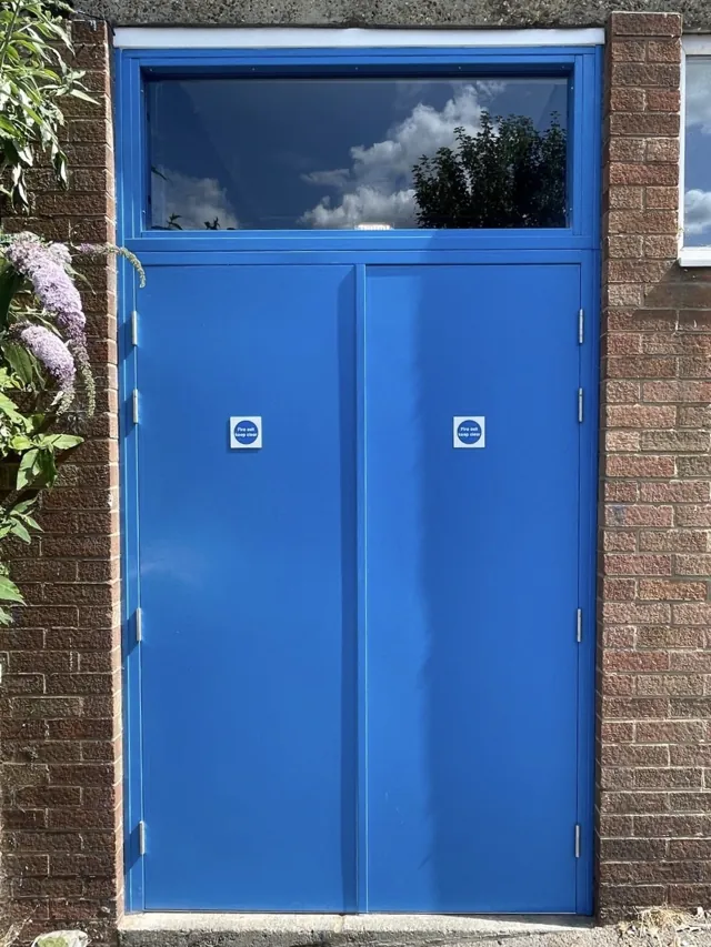 Blue entrance door with a glazed overlight and surrounding brickwork