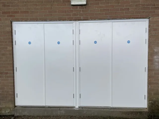 White painted multi-leaf door arrangement set in an exterior brick wall