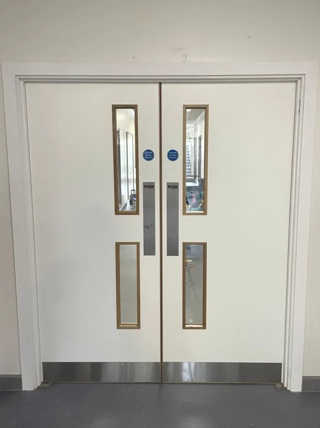 Cream-painted double doors with vertical glazing and metal lower protection plates