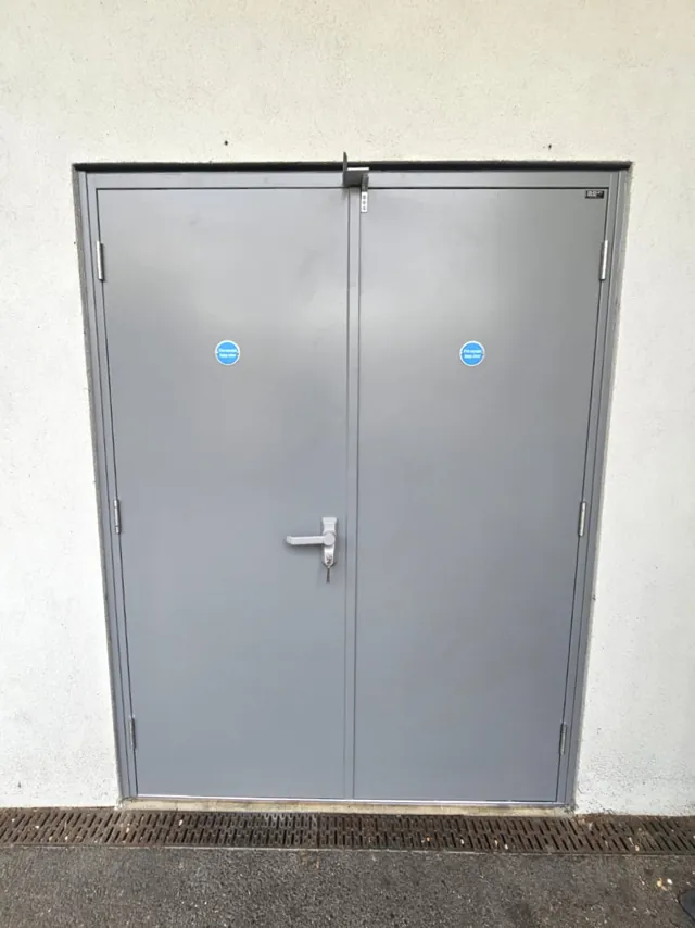 Grey double doors without glazing beneath a light-coloured wall