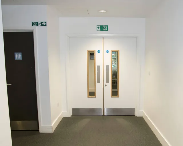 Wider corridor view of white double doors with narrow glazed panels