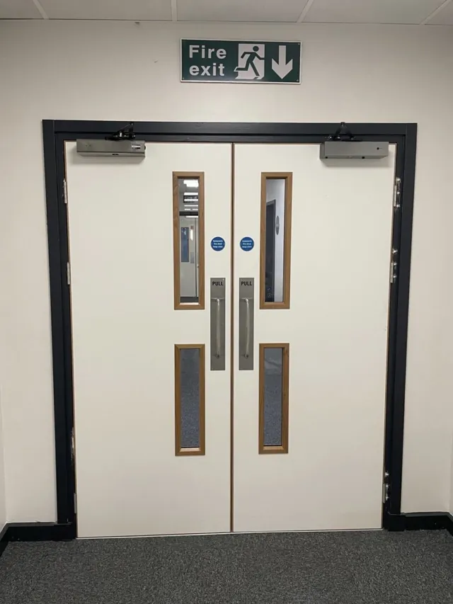 White double doors with vertical glazing and metal protection plates inside a dark frame