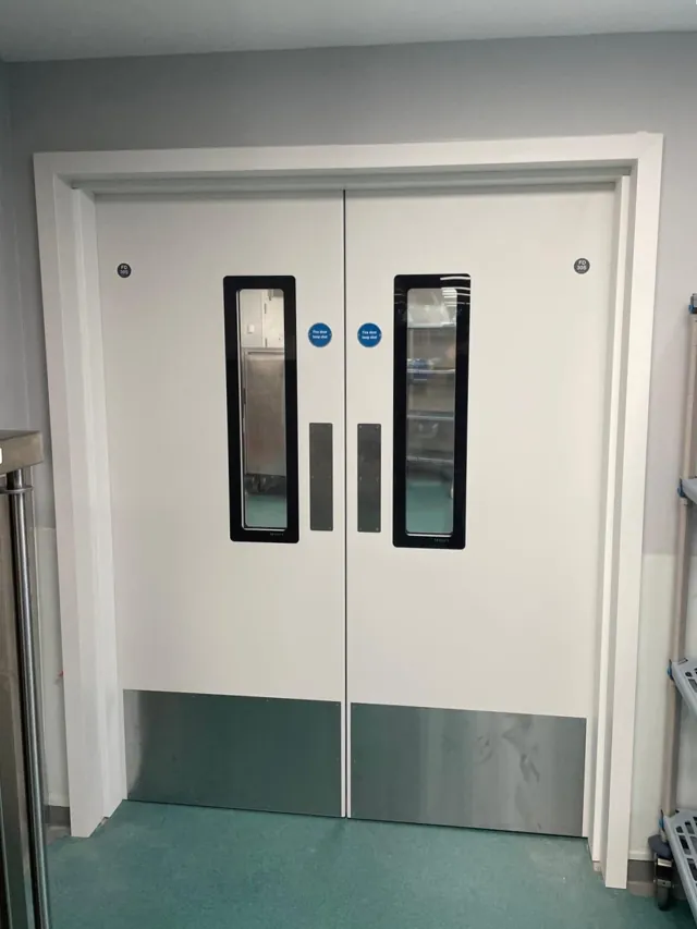White double doors with dark-edged vision panels and green lower protection panels