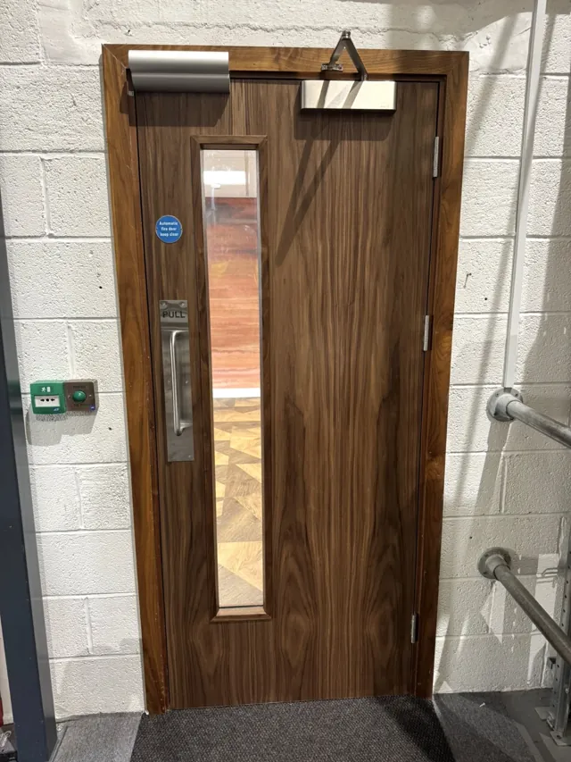 Dark timber single door with tall vision panel and overhead closer