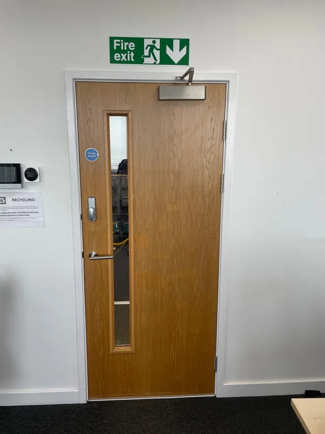 Oak-finish single door beneath an exit sign with overhead closer