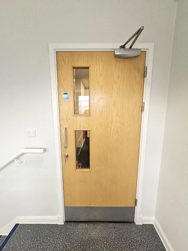 Pale timber single door with two vision panels and overhead closer