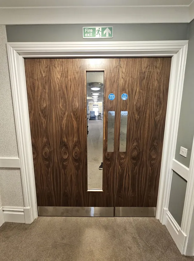 Dark veneer double doors with tall vision panels and overhead closers