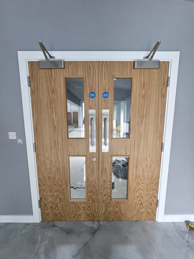 Oak-finish double doors with vision panels and overhead closers