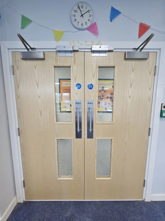 Pale timber double doors with vision panels beneath a clock and bunting