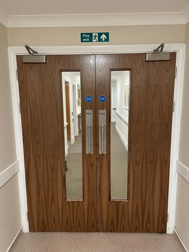 Timber double doors with tall glazed panels and overhead closers