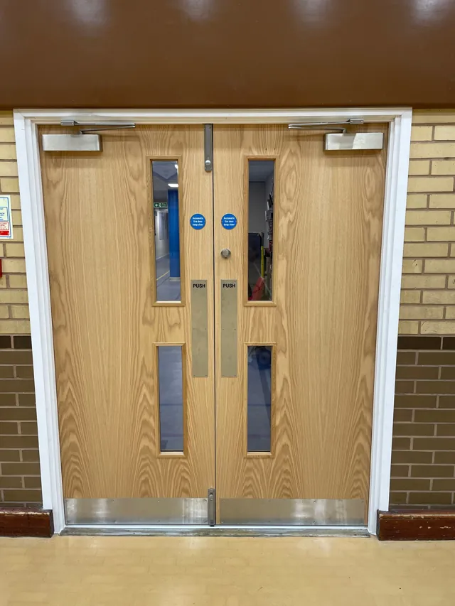 Timber double doors with vision panels below a red-brown panel